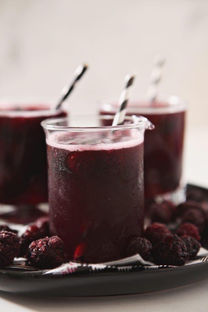 Close up of a Fizzy Potion Halloween Punch, garnished with frozen blackberries and a paper straw