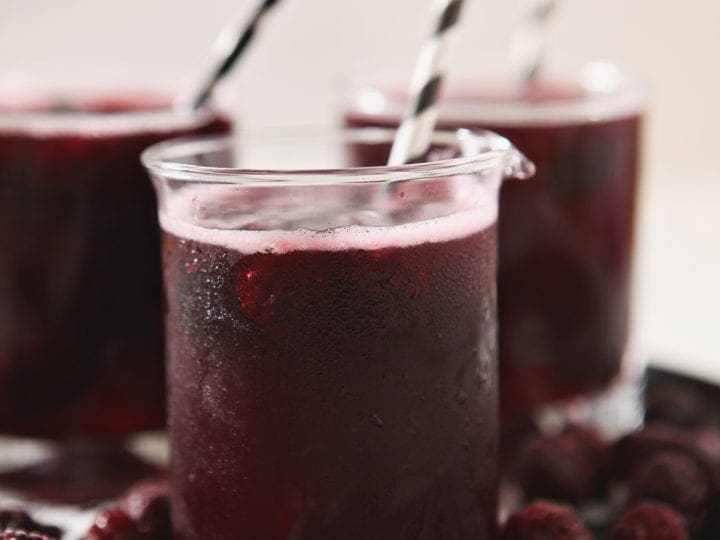 Close up of a Fizzy Potion Halloween Punch, garnished with frozen blackberries and a paper straw