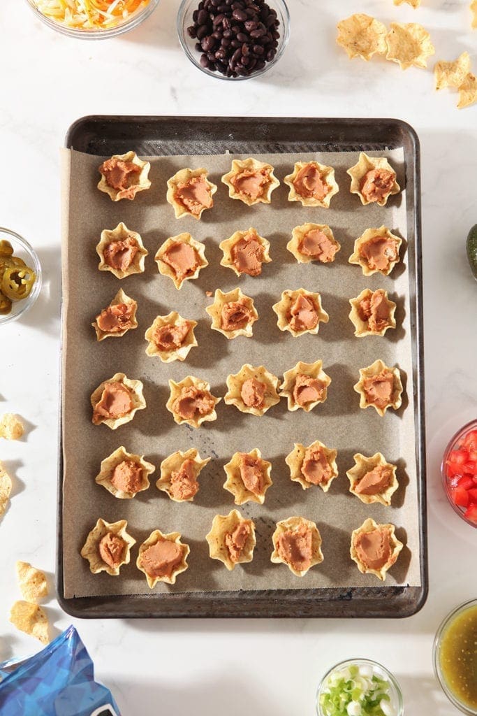 Tortilla chips on a baking sheet are filled with refried beans