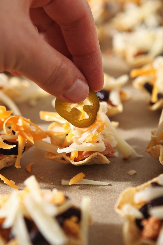 A woman places a pickled jalapeno on top of a nacho before baking