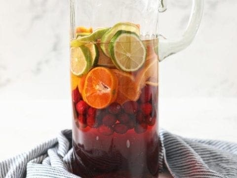 A pitcher holds oranges, limes, cranberries and ingredients for sangria