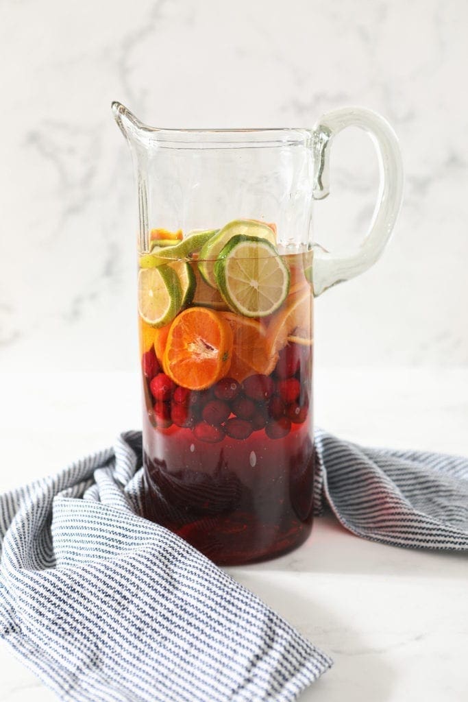 A pitcher holds oranges, limes, cranberries and ingredients for sangria