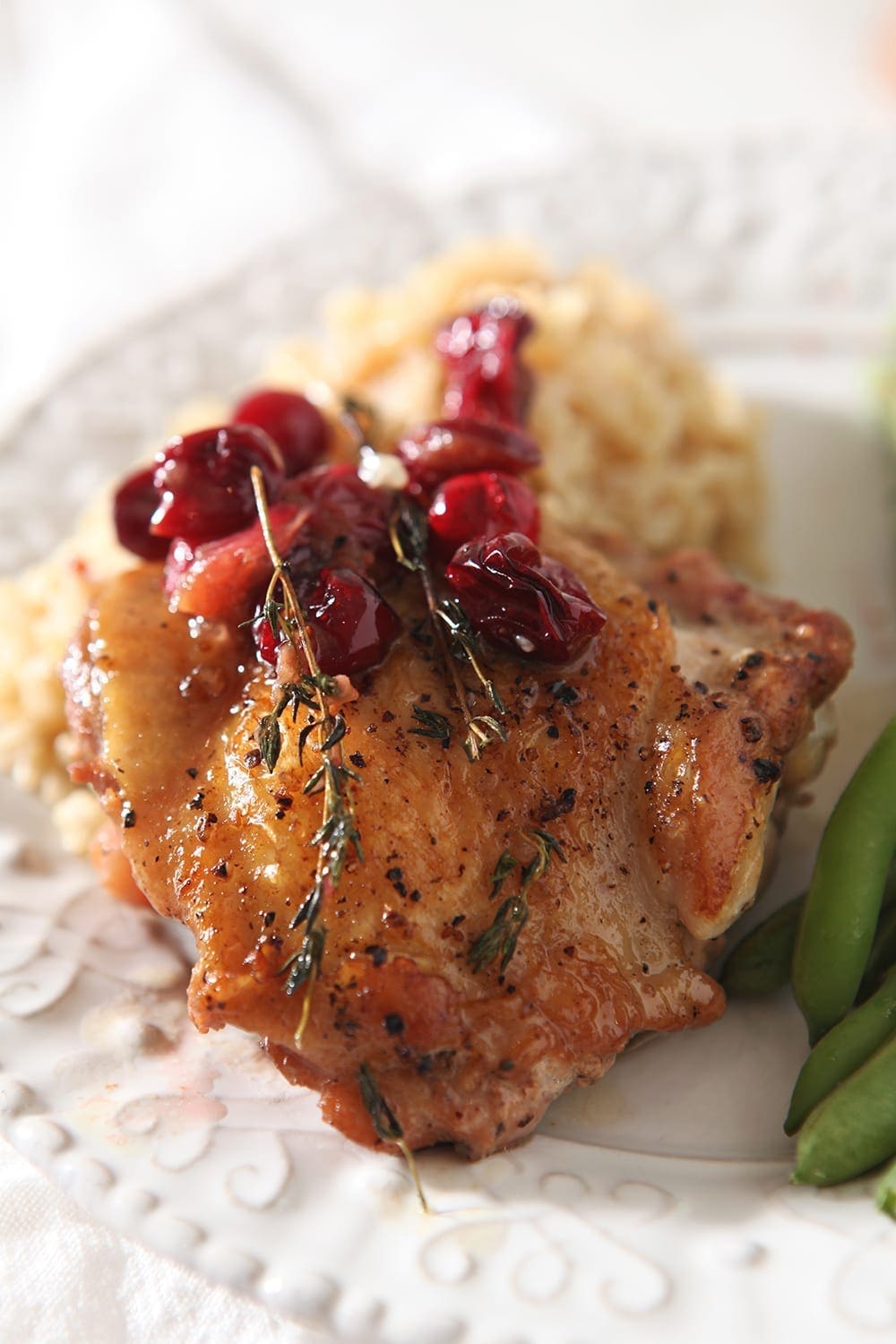 Close up of a Cranberry Chicken Thigh with brown rice and green beans on a plate