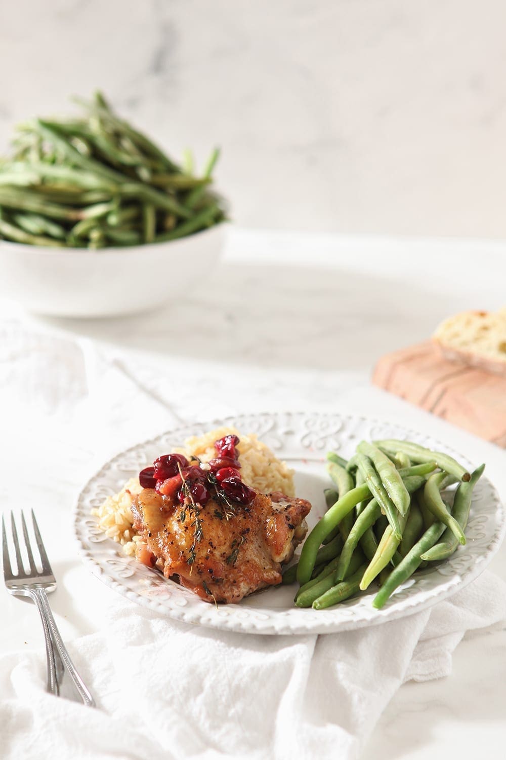 A cranberry chicken thigh is served on a white plate with steamed green beans