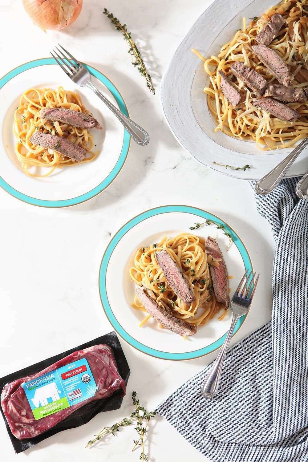 Overhead of pasta plates, with a Panorama ribeye beside them