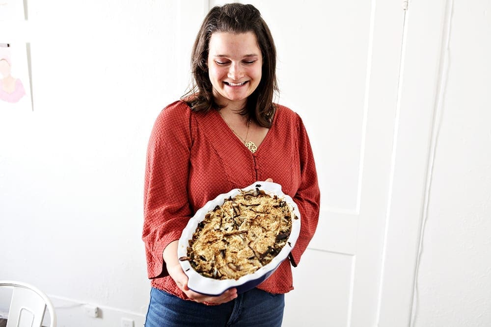 A woman in orange holds a casserole dish of Fresh Green Bean Casserole