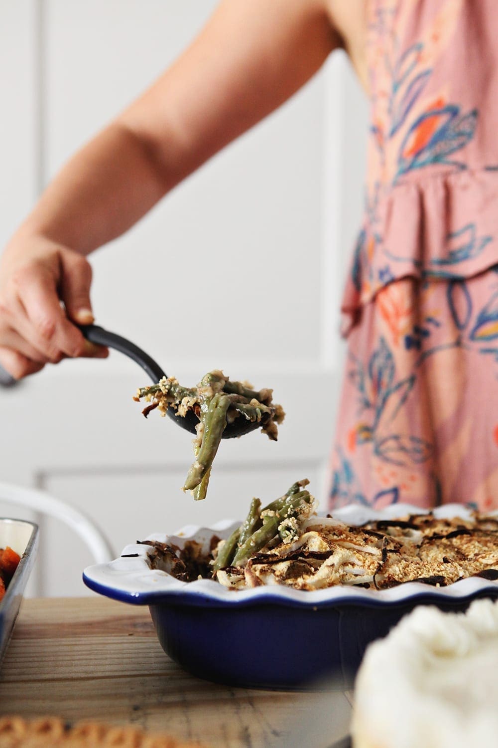 A woman lifts a spoon of Fresh Green Bean Casserole out of the dish