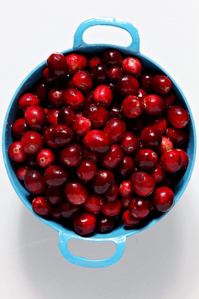 Cranberries sit in a blue colander, from above