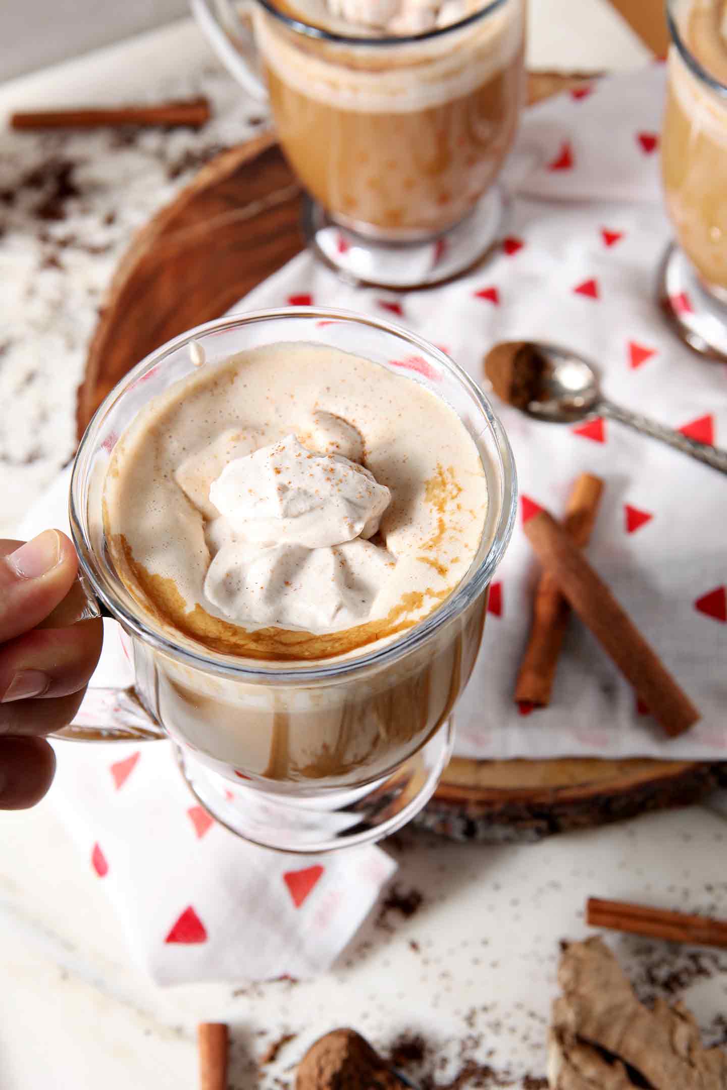 A person holds a mug of coffee with Gingerbread Coffee Creamer and Spiced Whipped Cream, above other mugs of the same