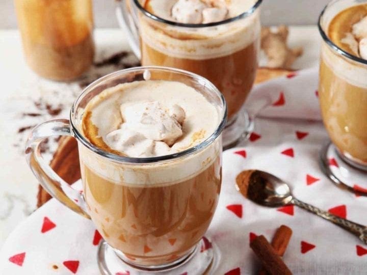 Three mugs of coffee with Homemade Gingerbread Coffee Creamer and spiced whipped cream sit on a marble surface, before drinking