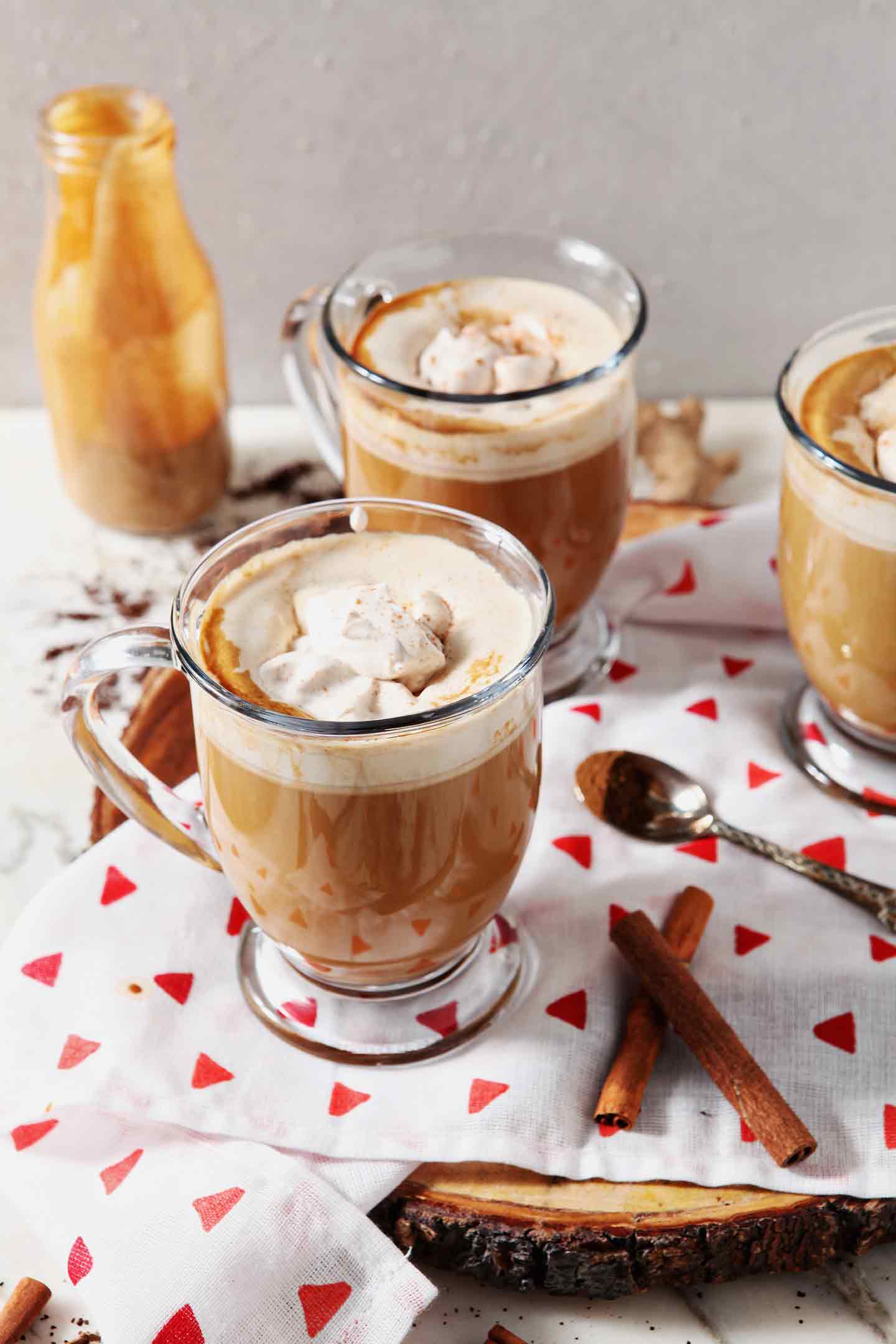 Three mugs of coffee with Homemade Gingerbread Coffee Creamer and spiced whipped cream sit on a marble surface, before drinking