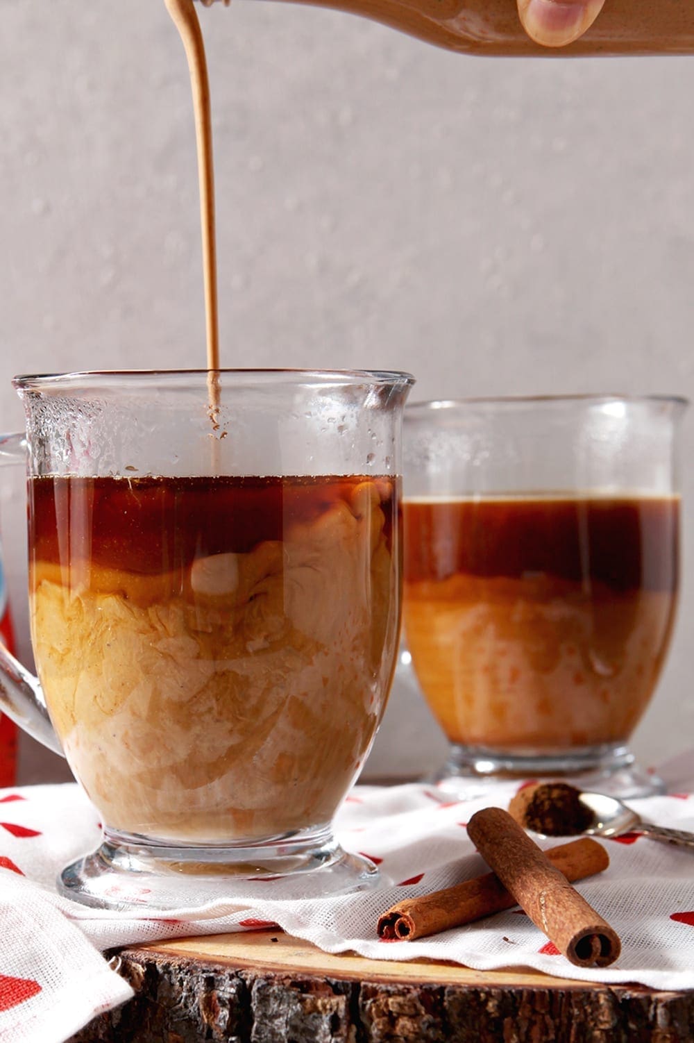 Creamer is poured into a clear glass mug of coffee