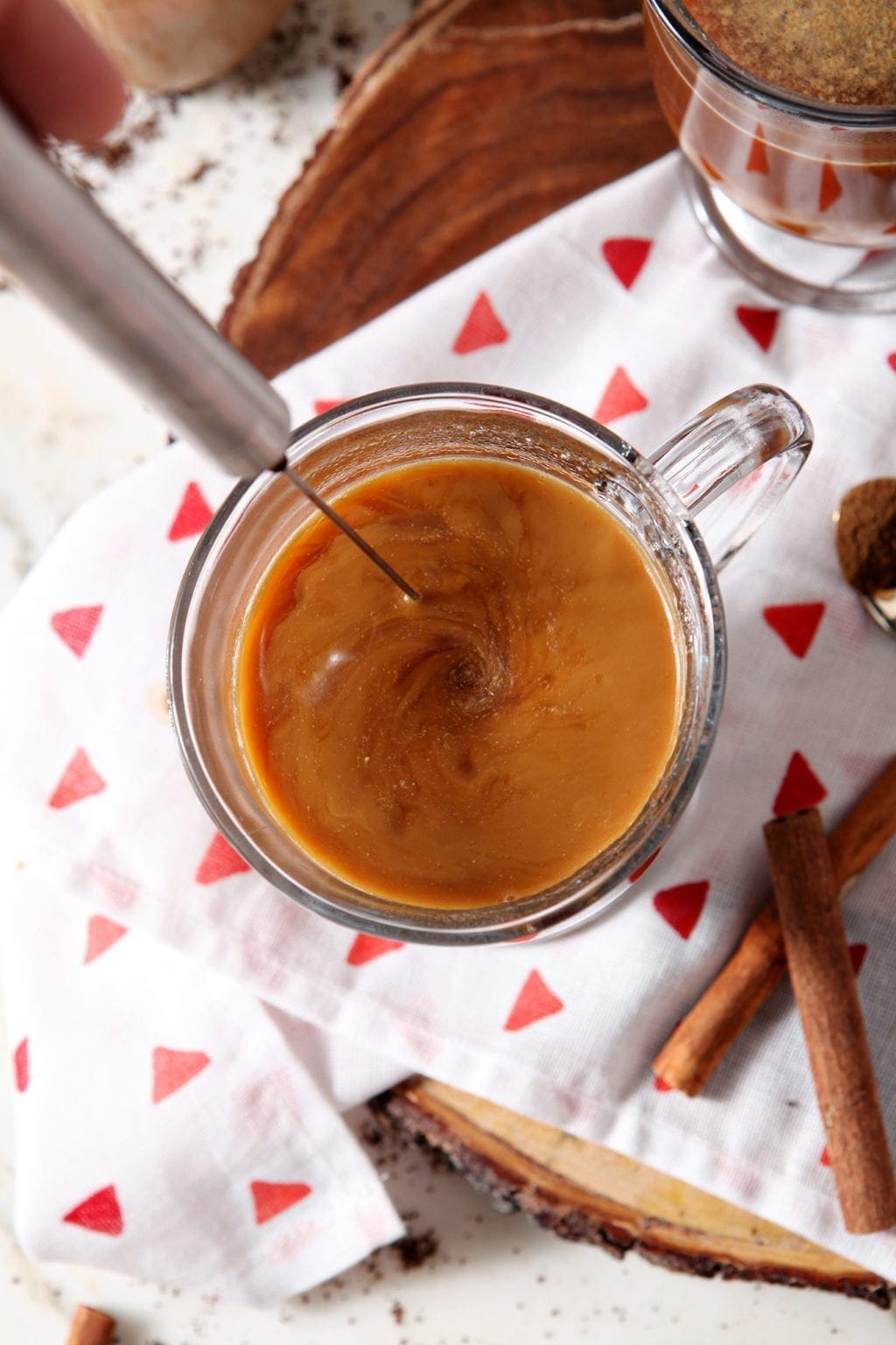 A frother mixes creamer into a glass of coffee, from above