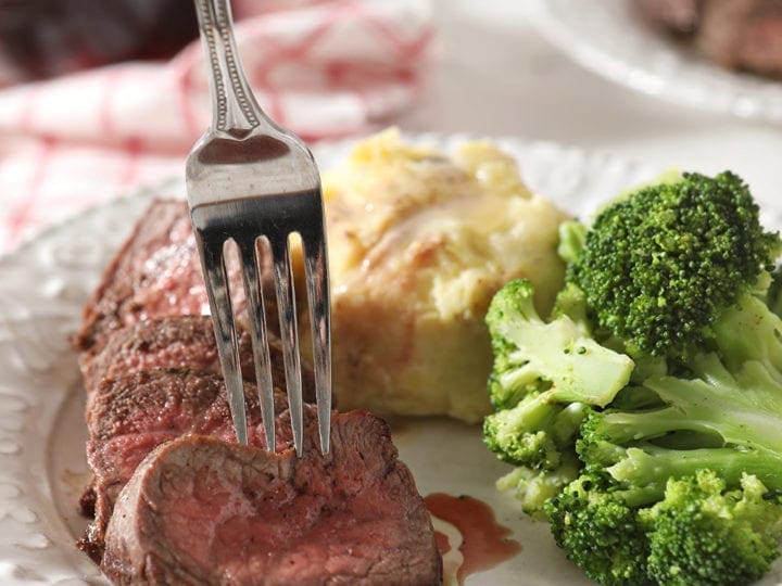 A fork sticks a sliced piece of steak before lifting it from the plate