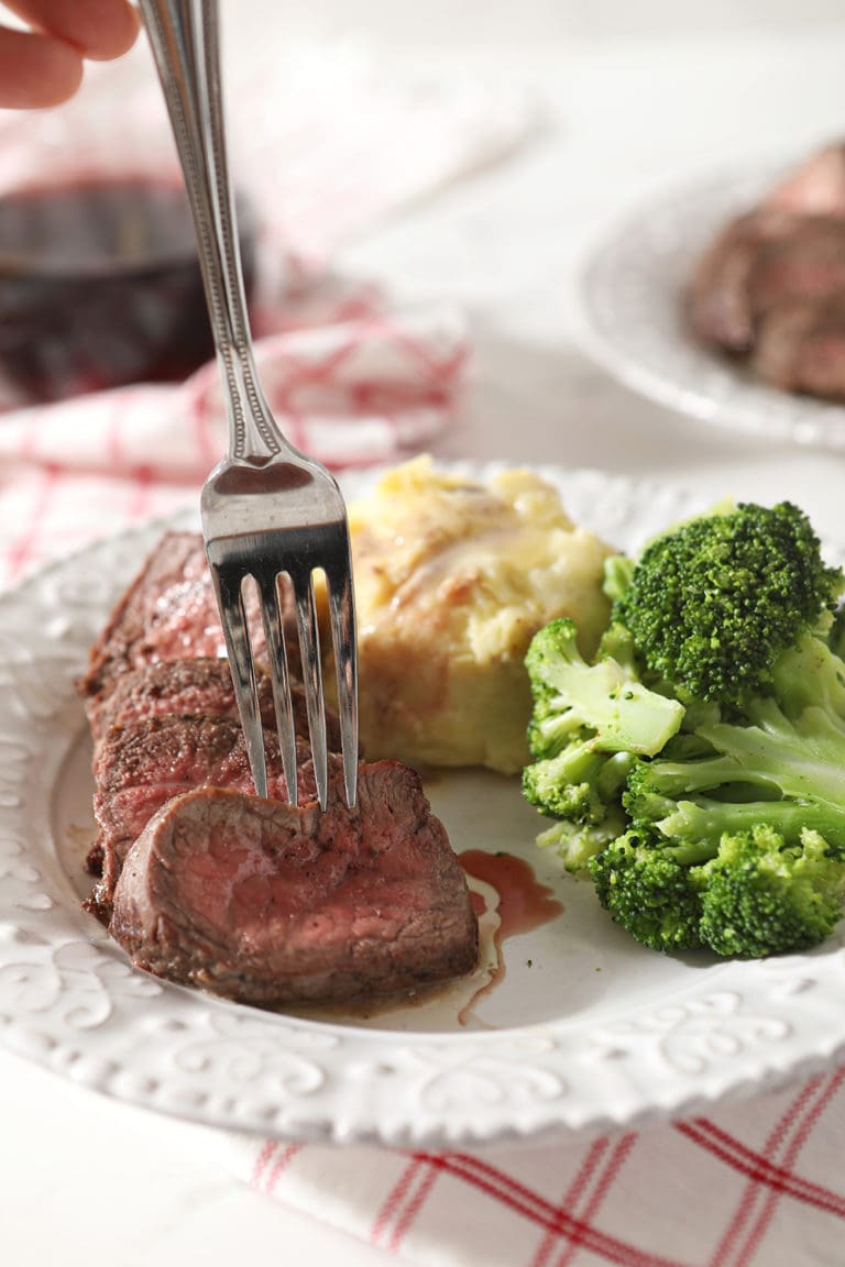 A fork sticks a sliced piece of steak before lifting it from the plate