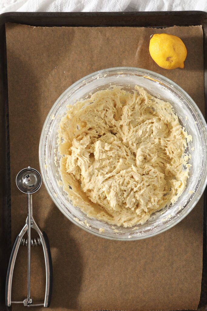 Lemon Drop Cookie batter, in a bowl, sits on top of a cookie sheet before scooping