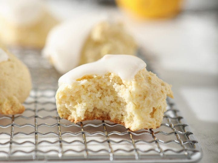 A lemon drop cookie, with a bite taken out of it, sits on a metal serving tray with other cookies