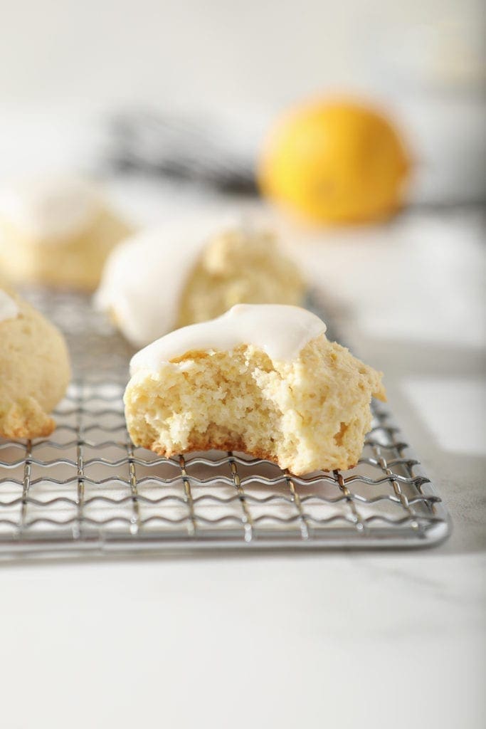 A lemon drop cookie, with a bite taken out of it, sits on a metal serving tray with other cookies