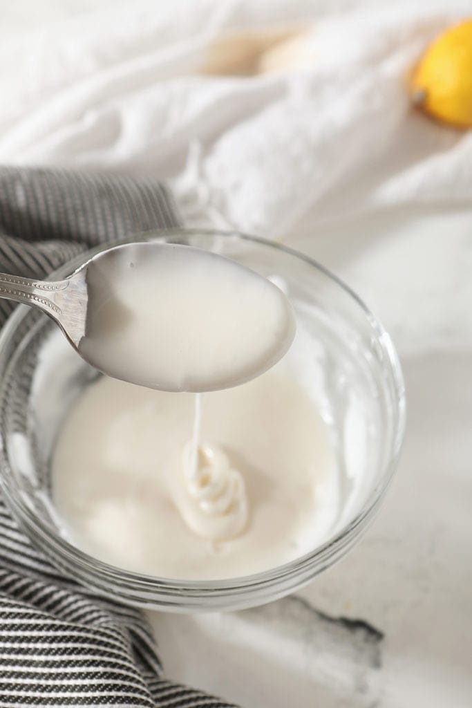 Lemon glaze drizzles off of a spoon into a bowl, from above