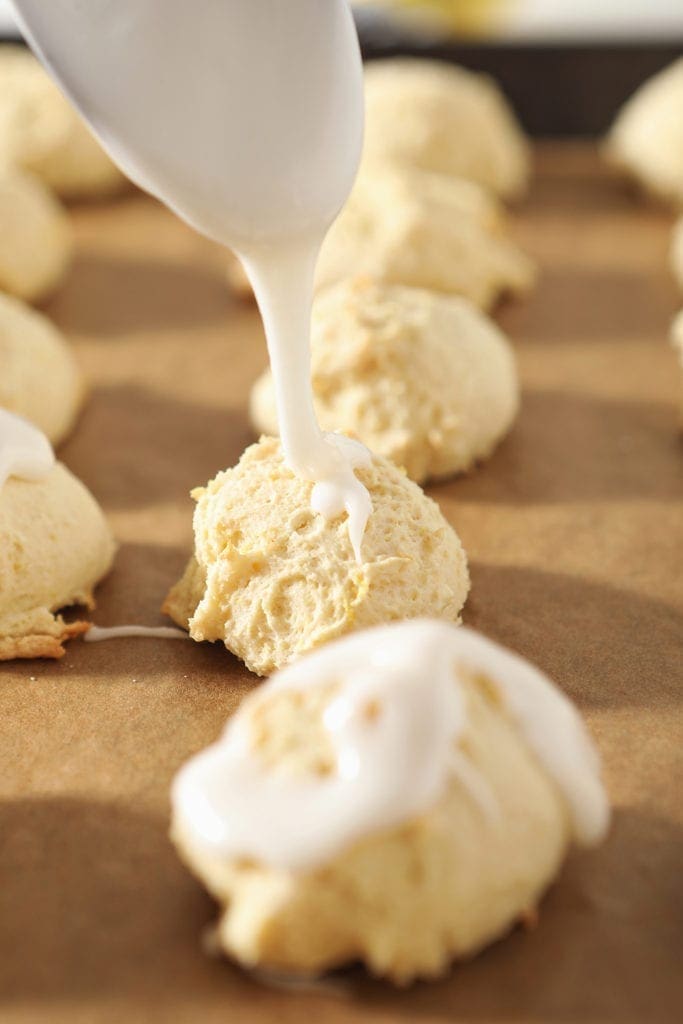 Glaze is drizzled onto a soft lemon cookie, lined up with other cookies on a baking sheet