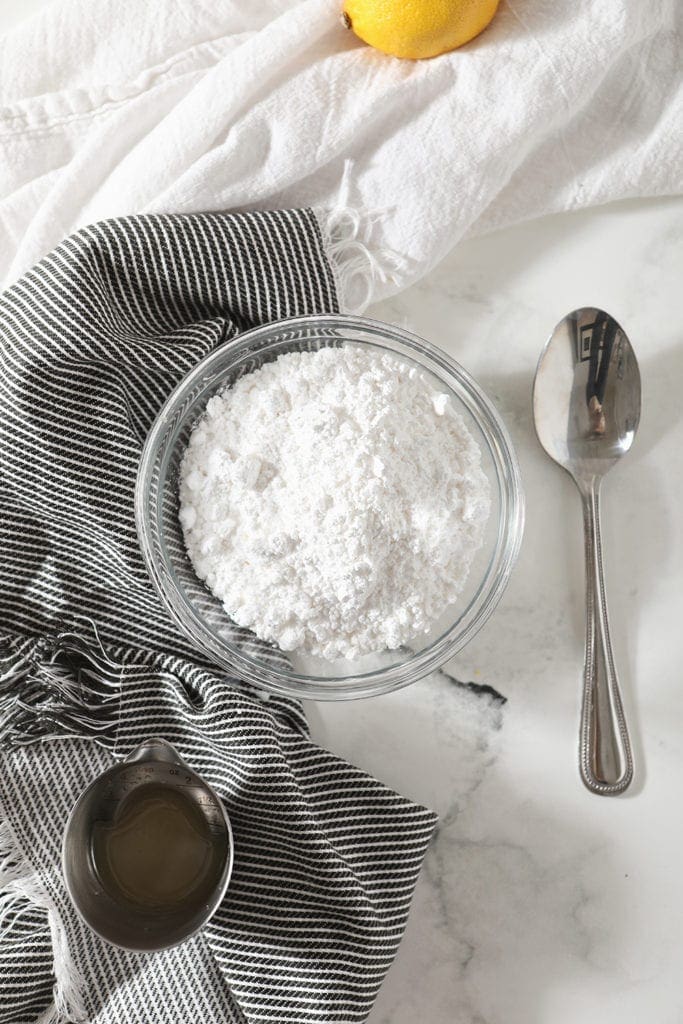 Powdered sugar and lemon juice for the glaze sit on top of a blue striped towel, before mixing