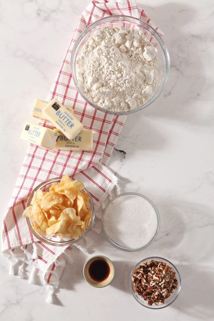 Ingredients for the cookies--butter, flour, potato chips, sugar, vanilla extract and pecans--are shown from above on a red plaid towel