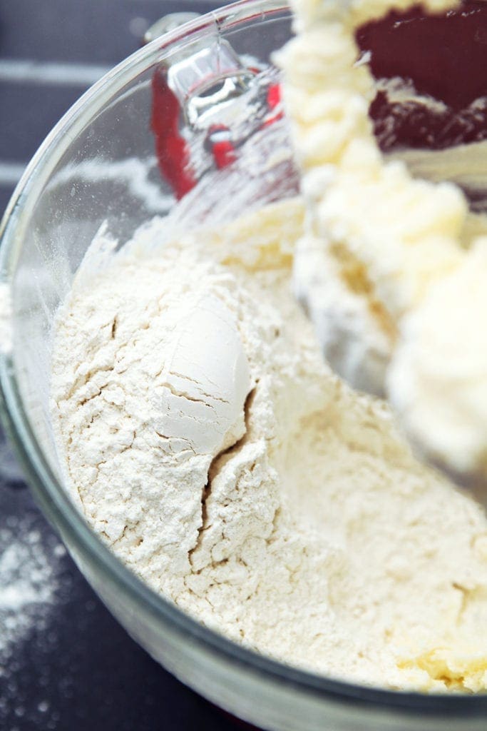 Flour sits atop creamed butter and flour in a mixer bowl