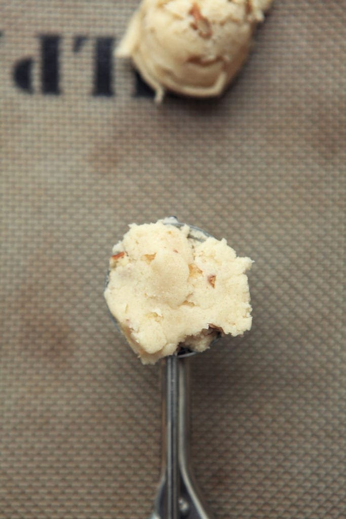 Cookie dough is shown in a cookie scooper, on a baking sheet