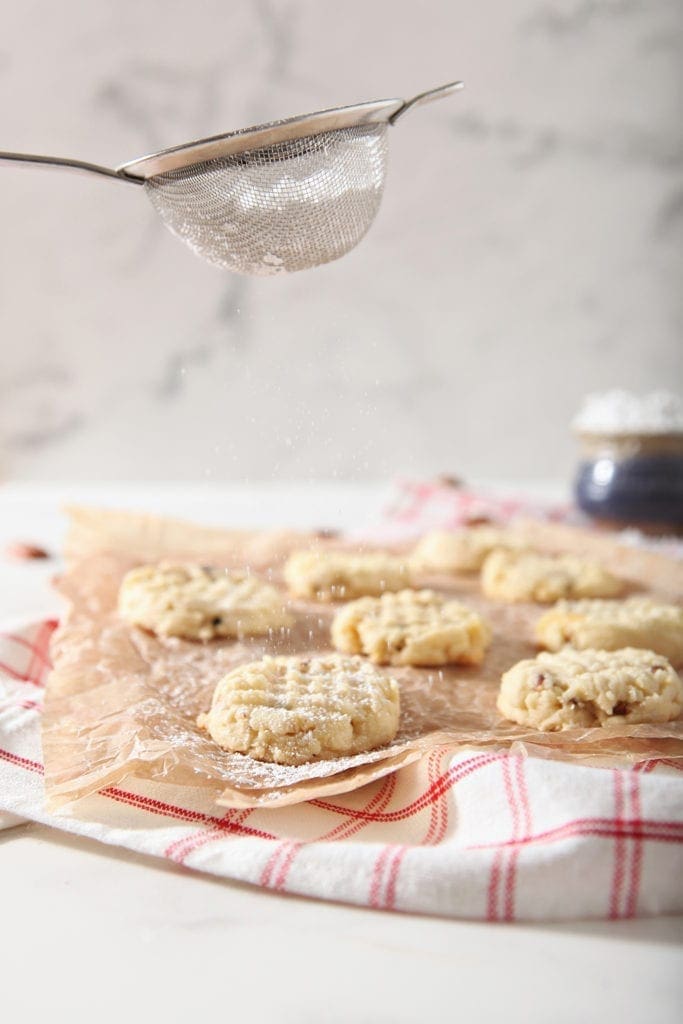 Powdered sugar is sprinkled on top of Potato Chip Cookies on parchment paper, after they've cooled