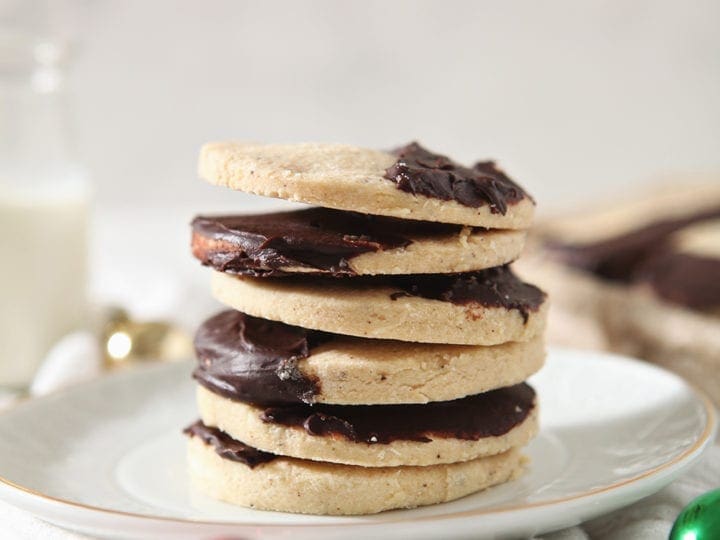 A stack of brown butter shortbread cookies on a white plate with a glass of milk
