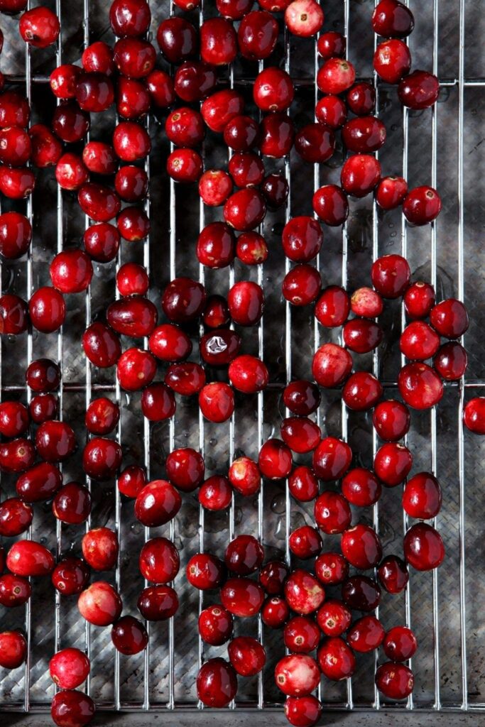 Cranberries, coated in simple syrup, sit on a cooling rack over a sheet pan