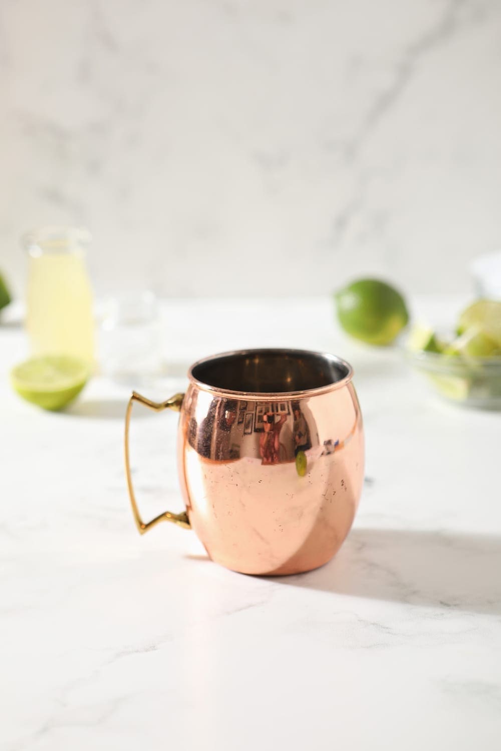 A copper mug sits on a marble countertop with drink ingredients scattered around it