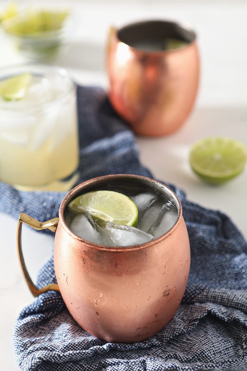 Close up of a copper mug holding a Moscow Mule, garnished with a lime, on a blue towel