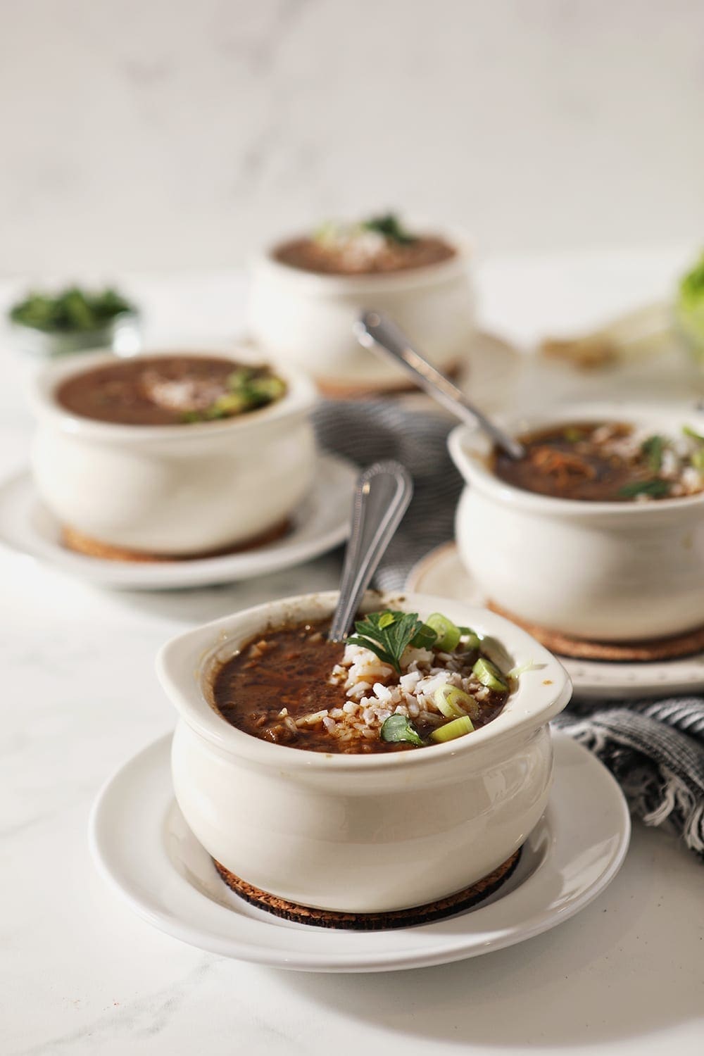 Four white bowls hold Instant Pot gumbo with rice and garnishes