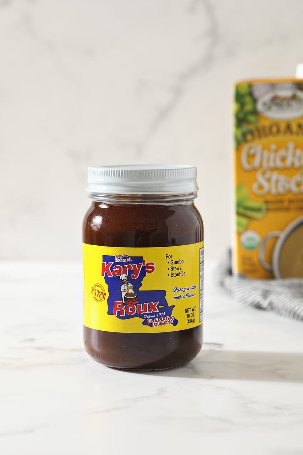 A jar of dark roux, in front of a box of chicken stock