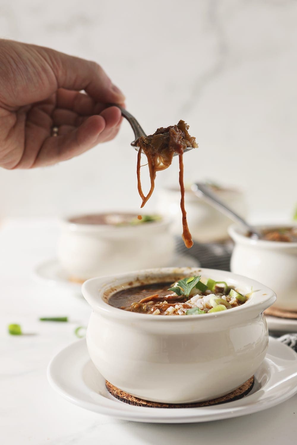 A person lifts a spoon of gumbo out of a bowl, with chicken spilling out of the spoon