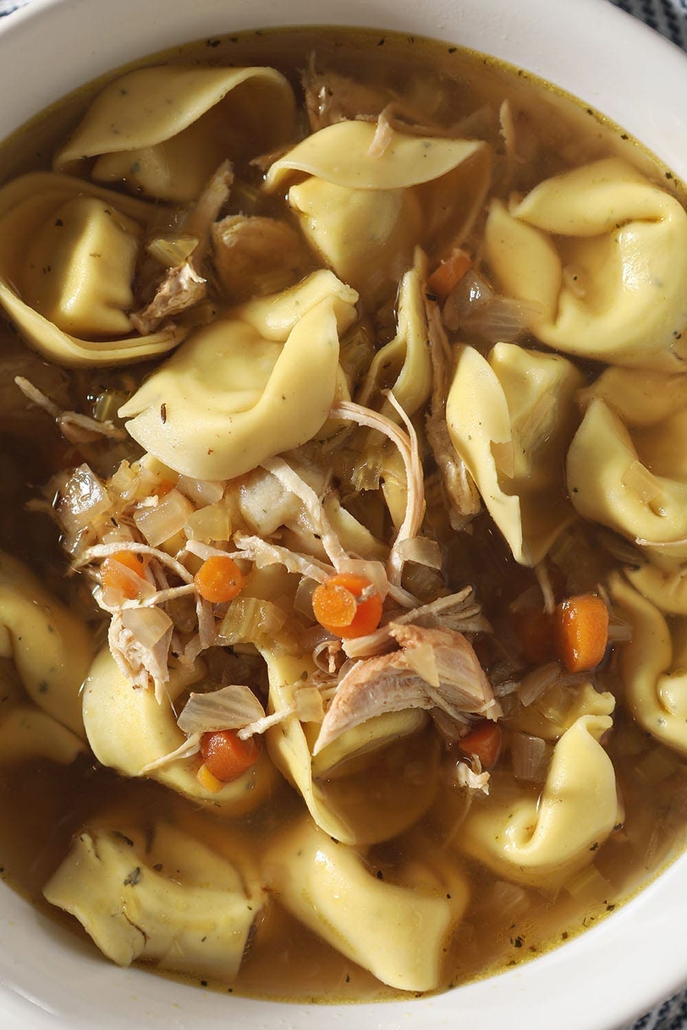 Close up of a bowl of Chicken Tortellini Soup, complete with shredded chicken