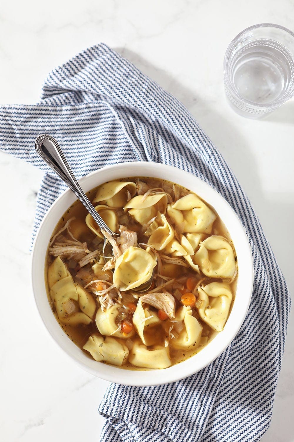 A white bowl holds Chicken Tortellini Soup, from above