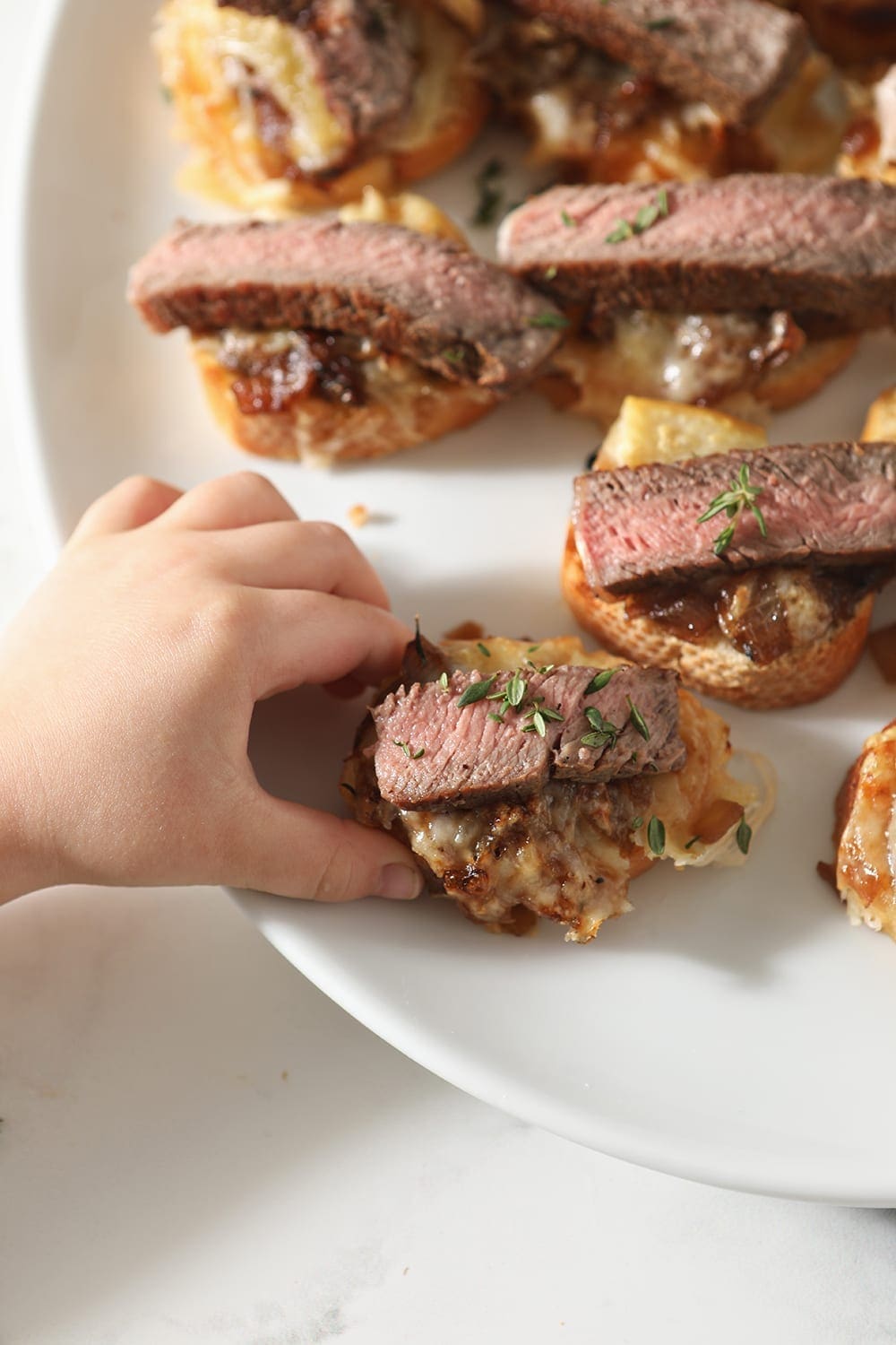 A girl grabs a Steak Bruschetta with French Onion Marmalade from a full white platter