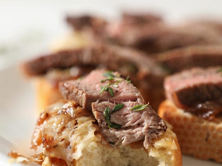 Close up of a bitten into Steak Bruschetta on a white platter with other bruschetta