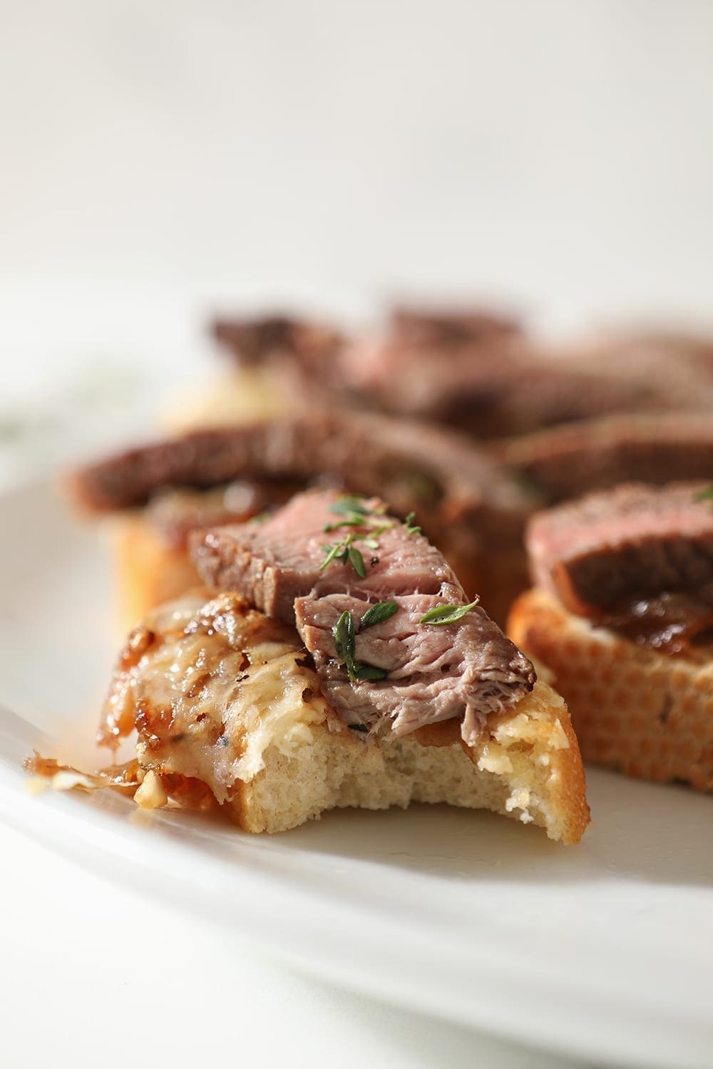 Close up of a bitten into Steak Bruschetta on a white platter with other bruschetta