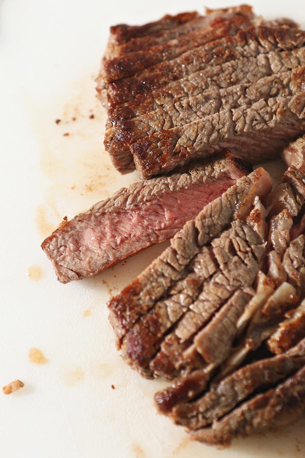 Sliced steak is shown from above on a white cutting board