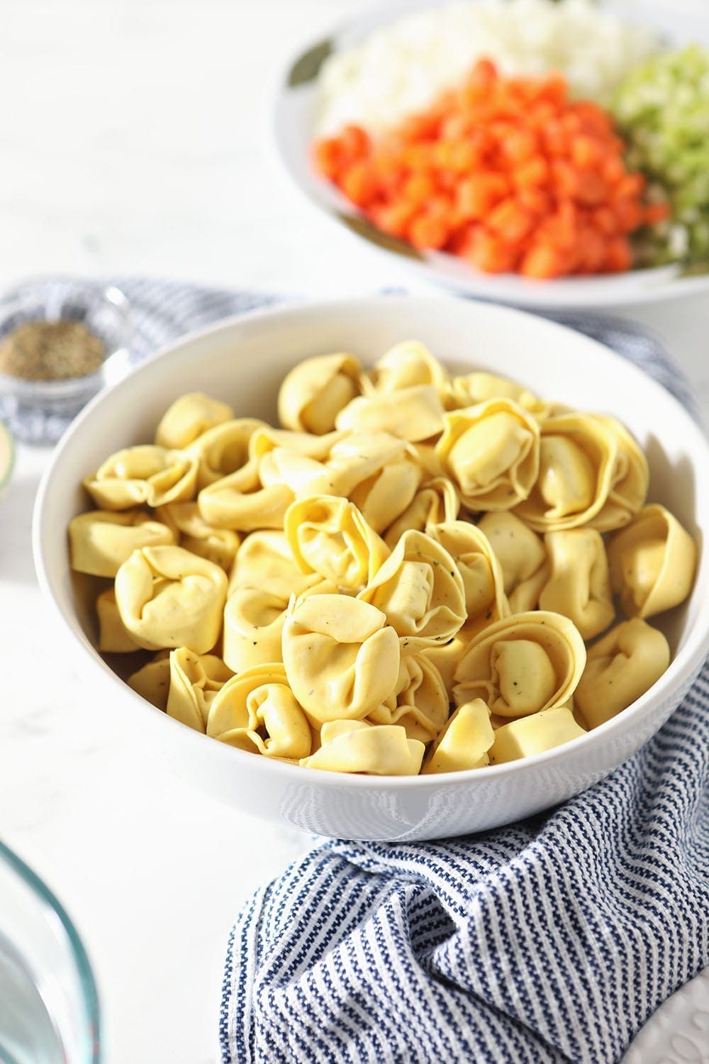 A bowl of cheese tortellini sits on a striped blue towel