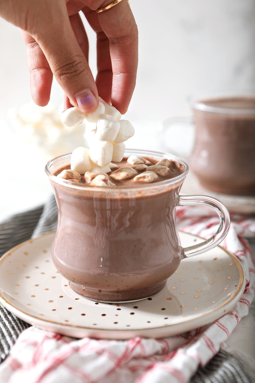 A woman drops miniature marshmallows on top of a mug of homemade hot cocoa