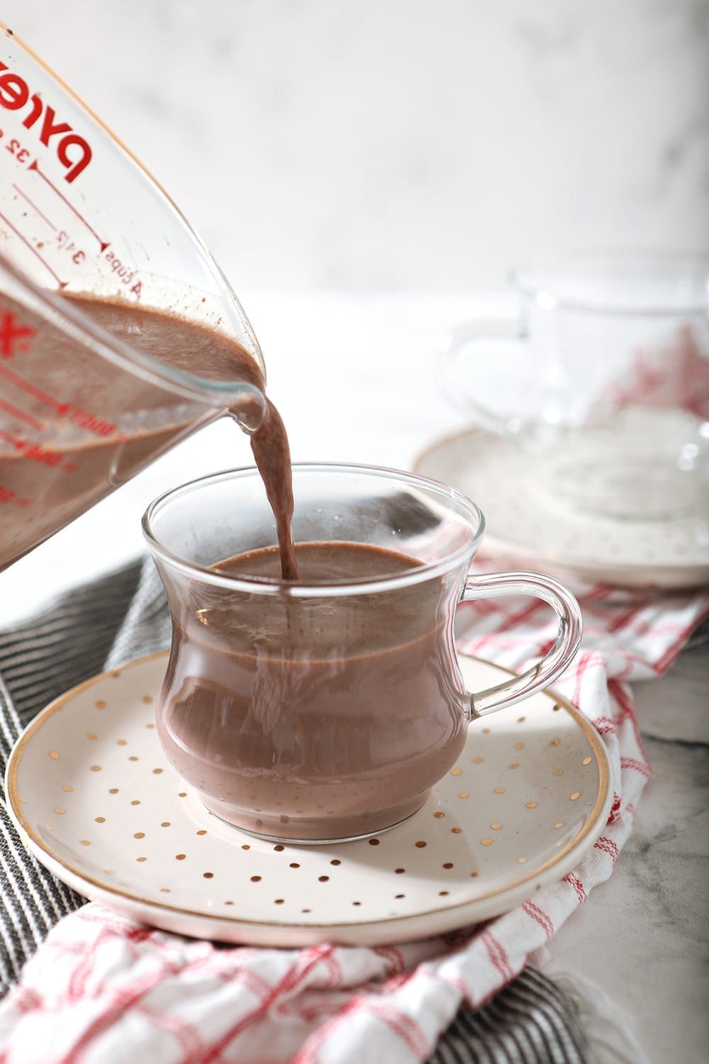 Gourmet Hot Chocolate is poured into a clear mug on a golden polka dot plate