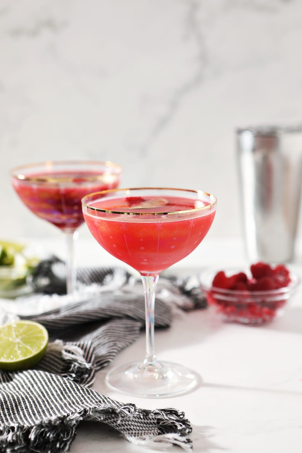 Two Raspberry Mules are shown on a marble background, with a striped blue cloth, limes and raspberries