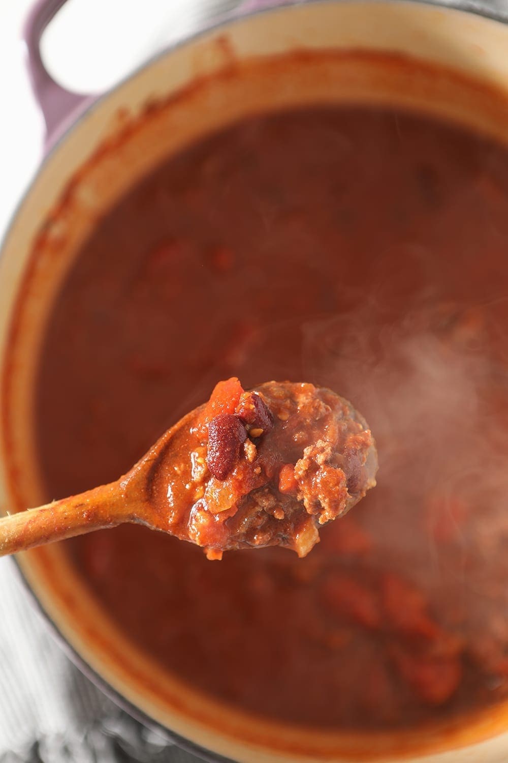 A wooden spoon lifts Beer Chili out of the Dutch oven, from above