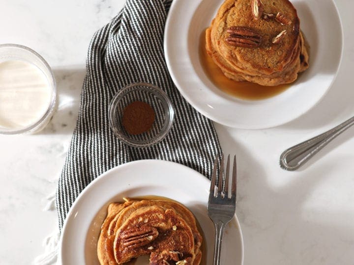 Overhead of two white plates holding stacks of Sweet Potato Pancakes, one with a bite taken out of it