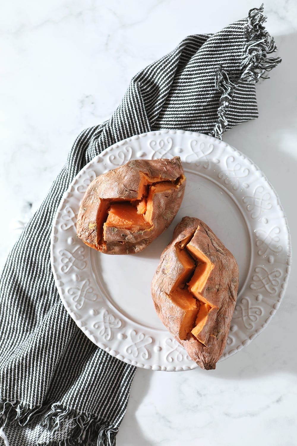 Two cooked sweet potatoes, sliced open, are shown on a white plate from above