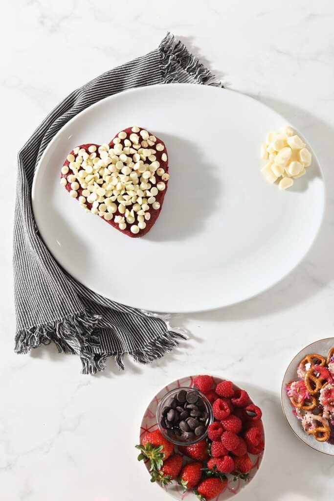 A heart-shaped dessert cheese ball sits on a white platter with cheese rounds